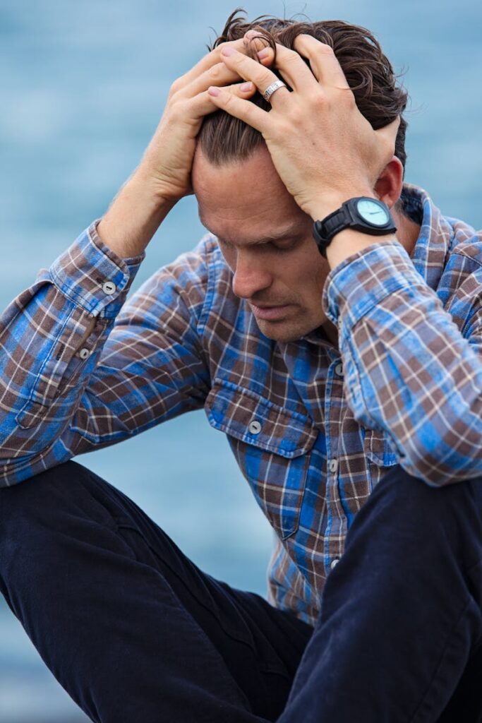 pexels-photo-897817-897817 A man in a plaid shirt sits by the water looking distressed, symbolizing stress.